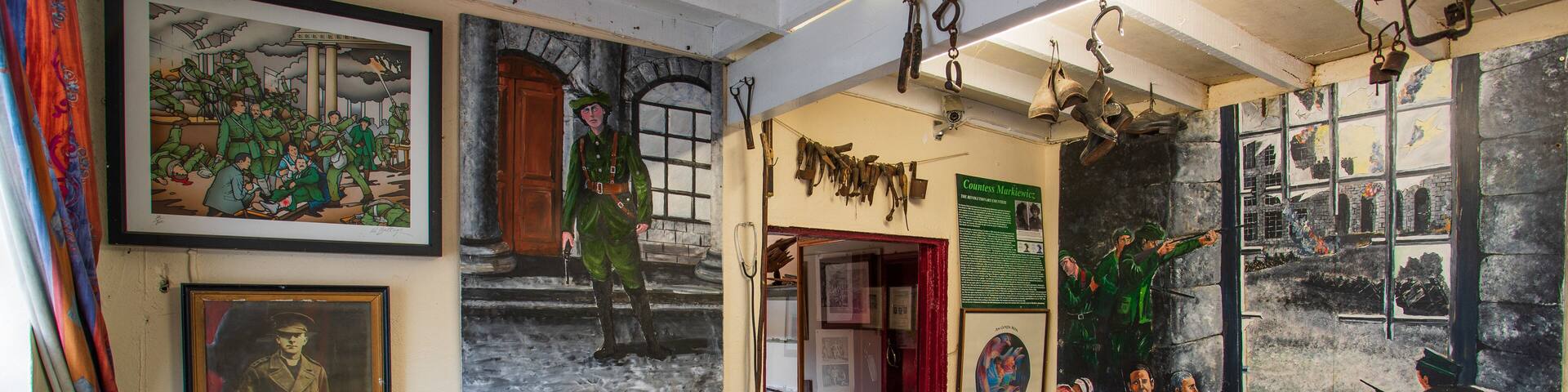 A gallery with various framed artworks, including paintings and photographs, and a large mural depicting a historical scene.