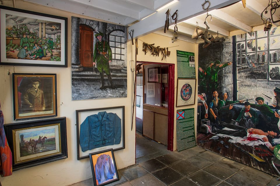 A gallery with various framed artworks, including paintings and photographs, and a large mural depicting a historical scene.