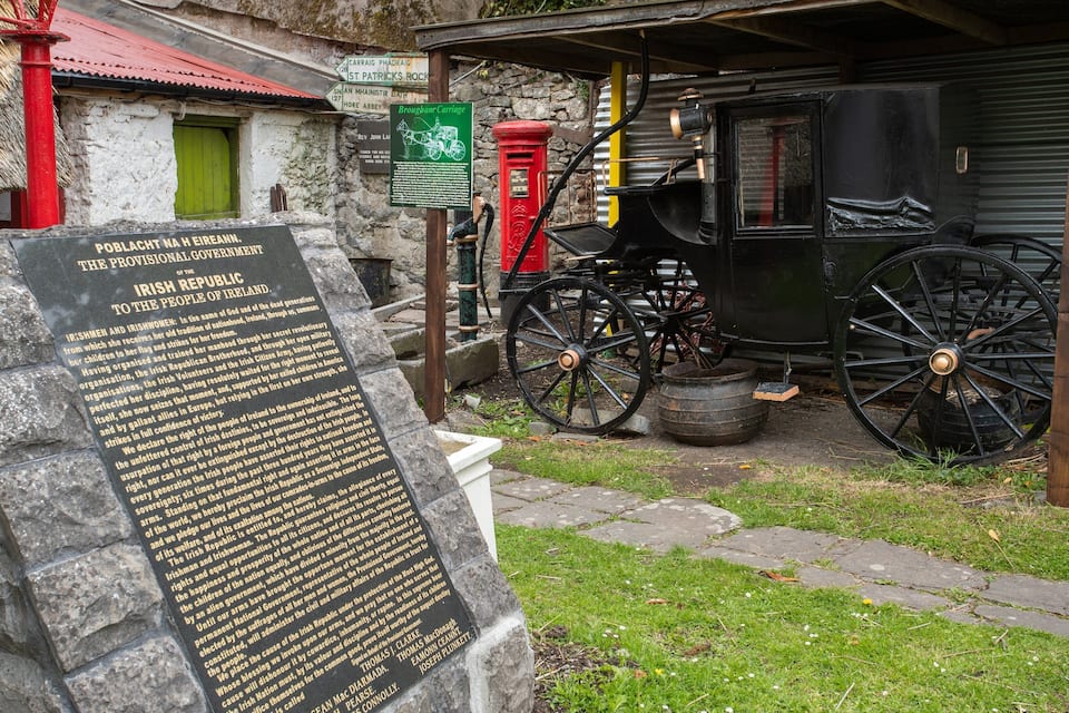 Une exposition historique comprenant une plaque commémorative en pierre, un attelage d’époque et une boîte aux lettres rouge.