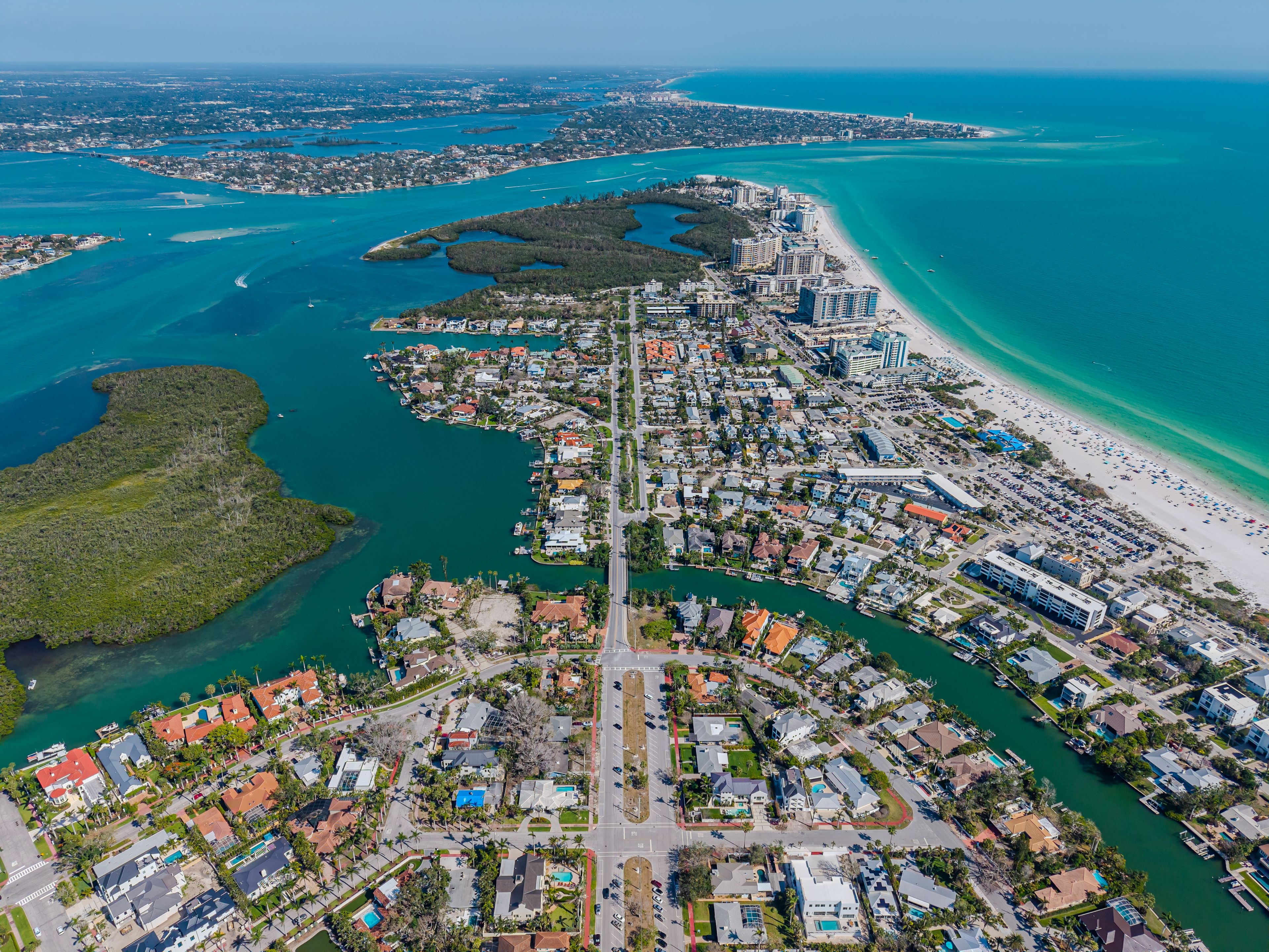 An aerial view of a coastal city with a dense urban area, a long beachfront, and a network of waterways.