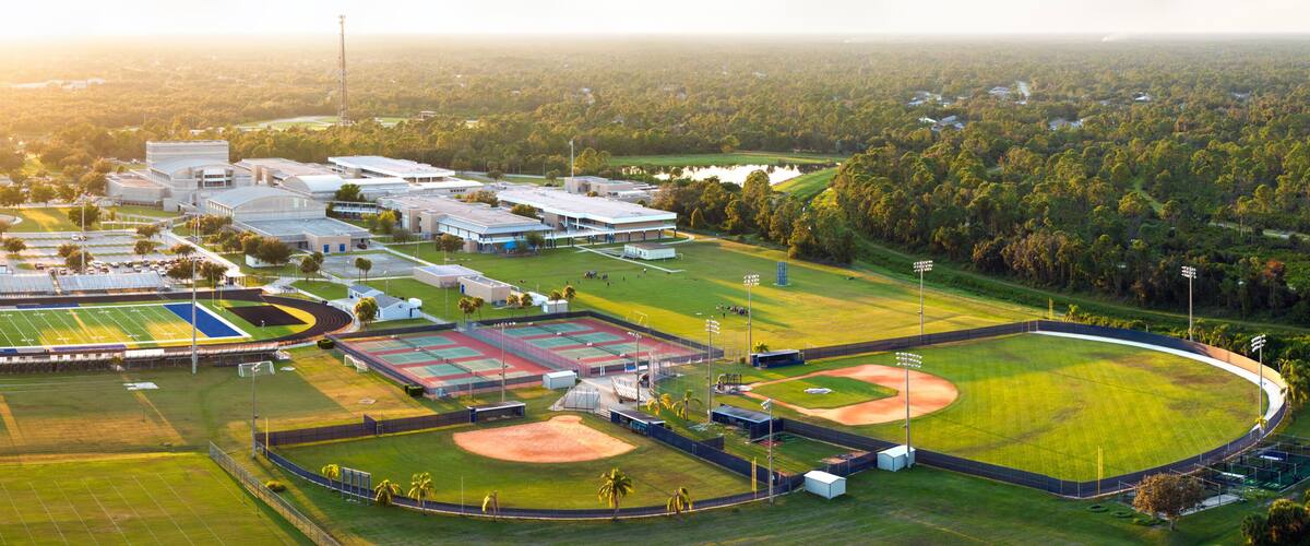 An aerial view of a sports complex with multiple fields, buildings, and surrounding forest.