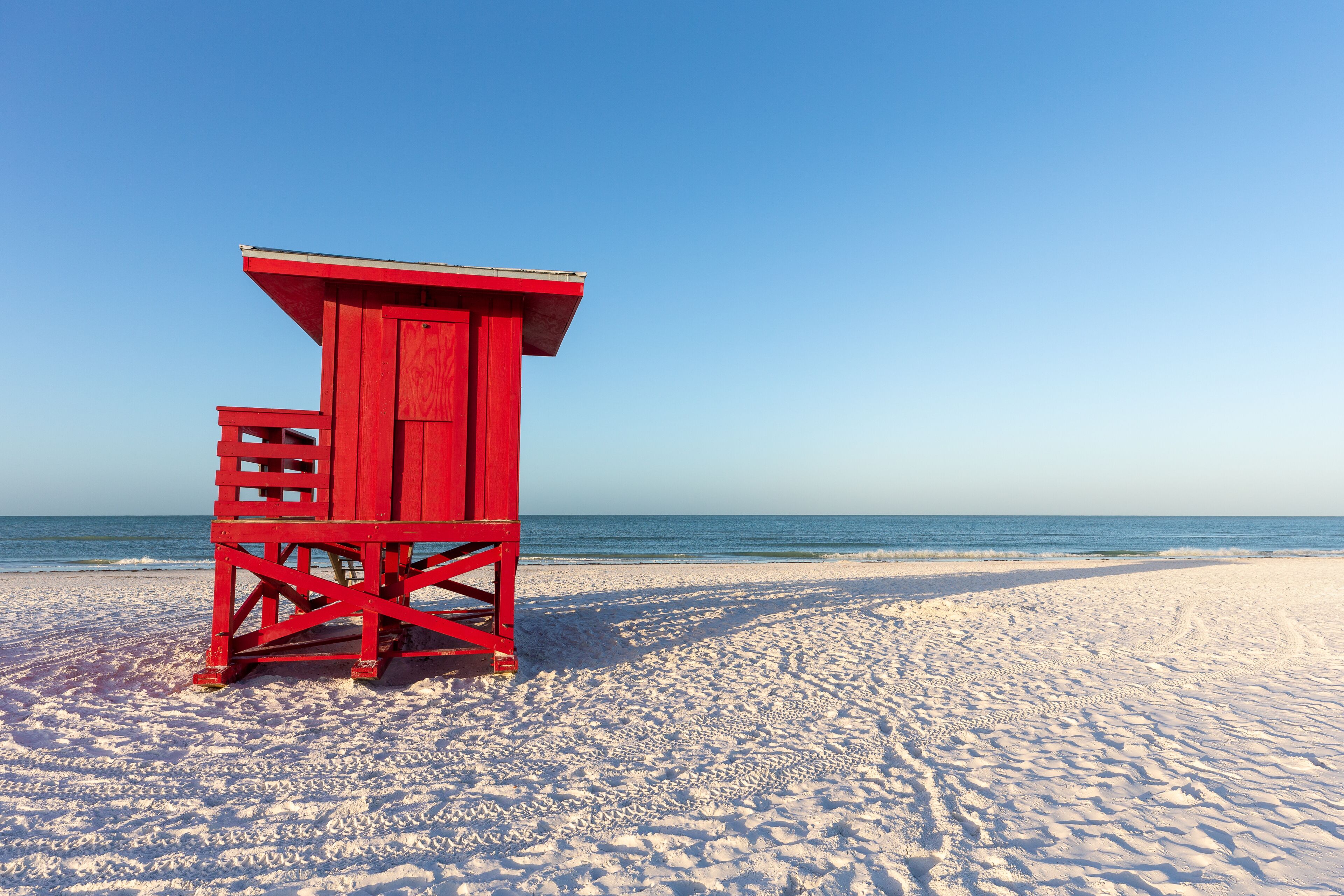 A red lifeguard tower on a sandy beach with the ocean in the background.