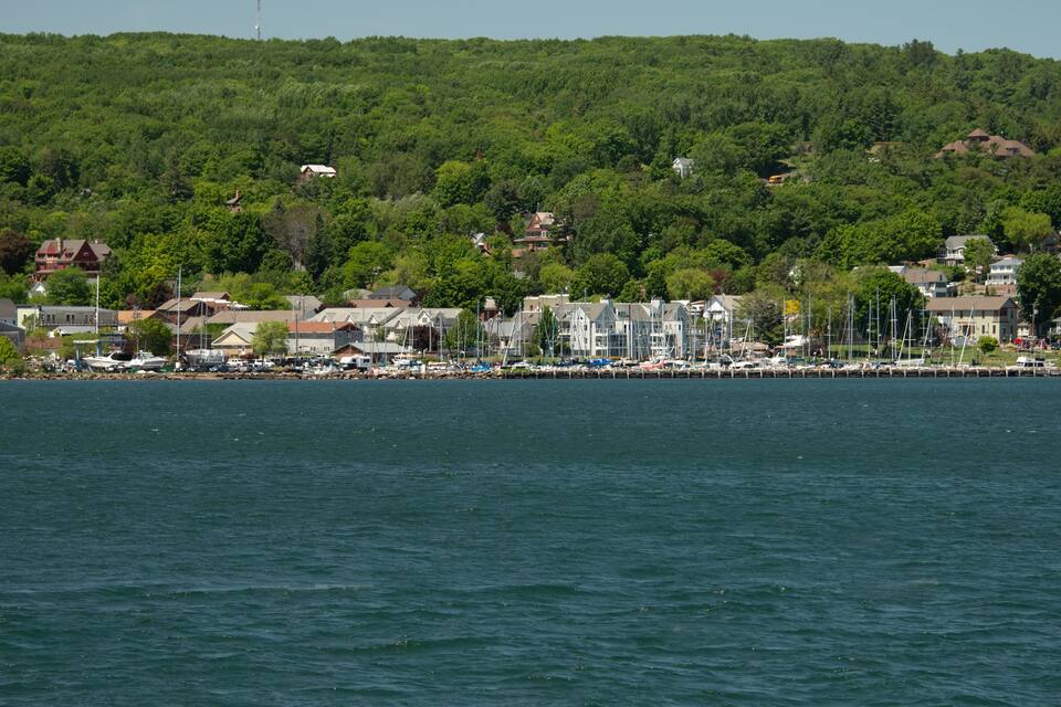 Une ville côtière dotée d’un port de plaisance, de maisons et, en arrière-plan, d’une colline boisée.