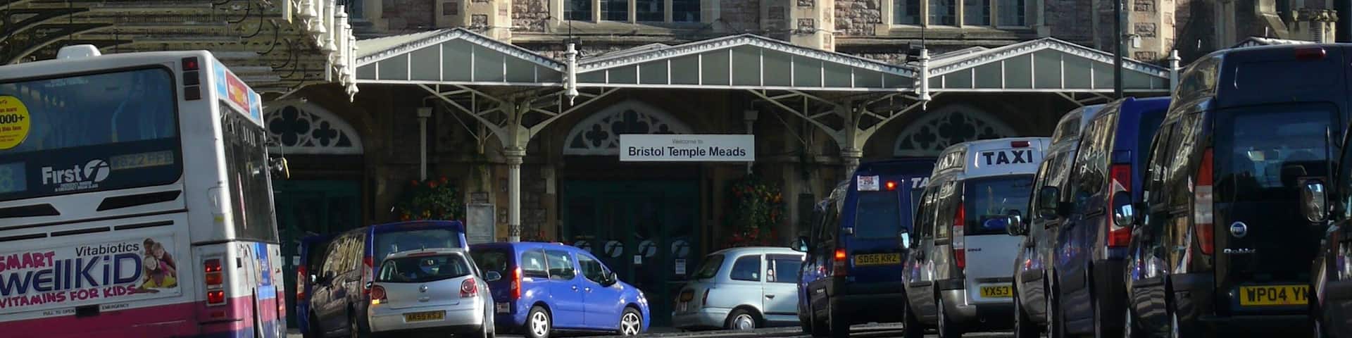 A historic building with a clock tower, surrounded by parked cars and buses.