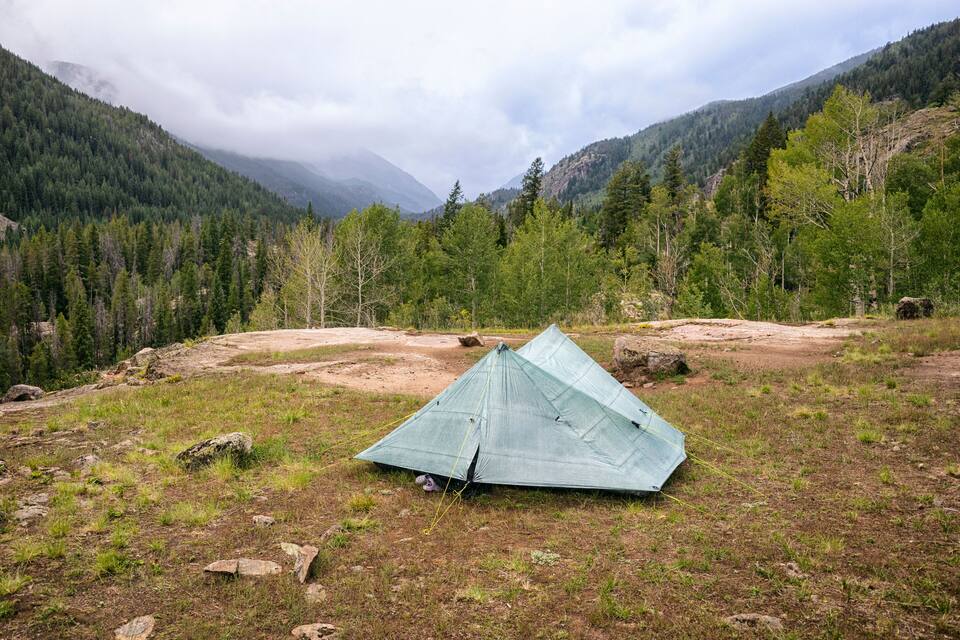 A blue tent in a grassy field with mountains in the background.