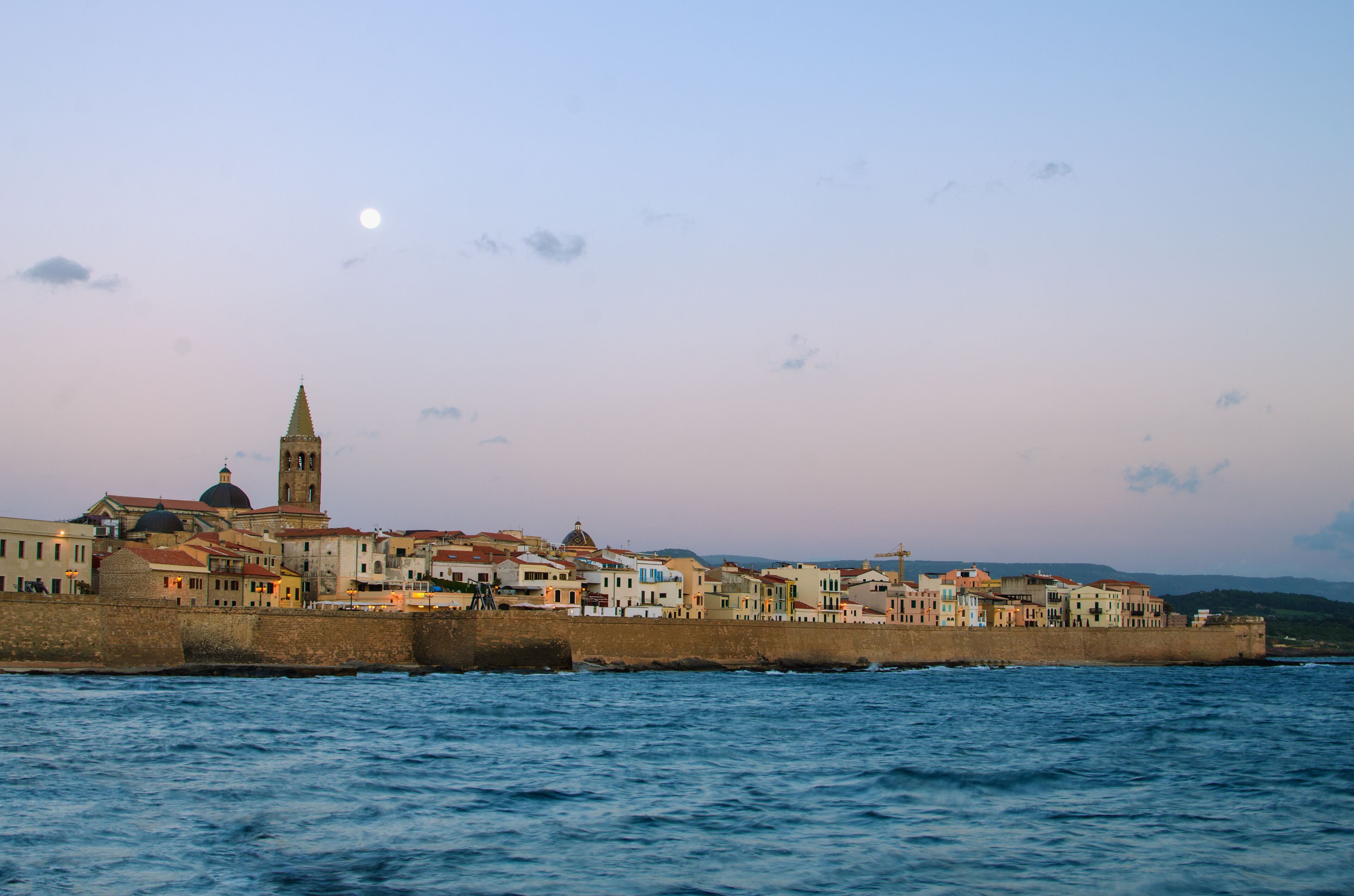 Old Town of Alghero (Sardinia Island, Italy) in the moonlight of sunset. Defensive wall of the city. The view from Mediterranean sea.