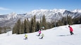 Une piste de ski enneigée avec des skieurs, un télésiège et des montagnes recouvertes de neige en arrière-plan.