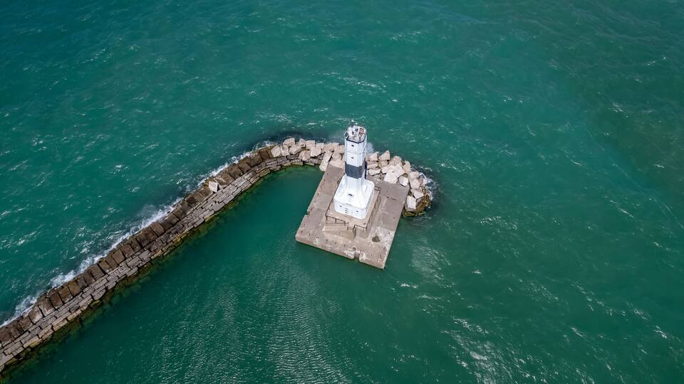 An aerial view of a lighthouse on a small island with a stone breakwater.