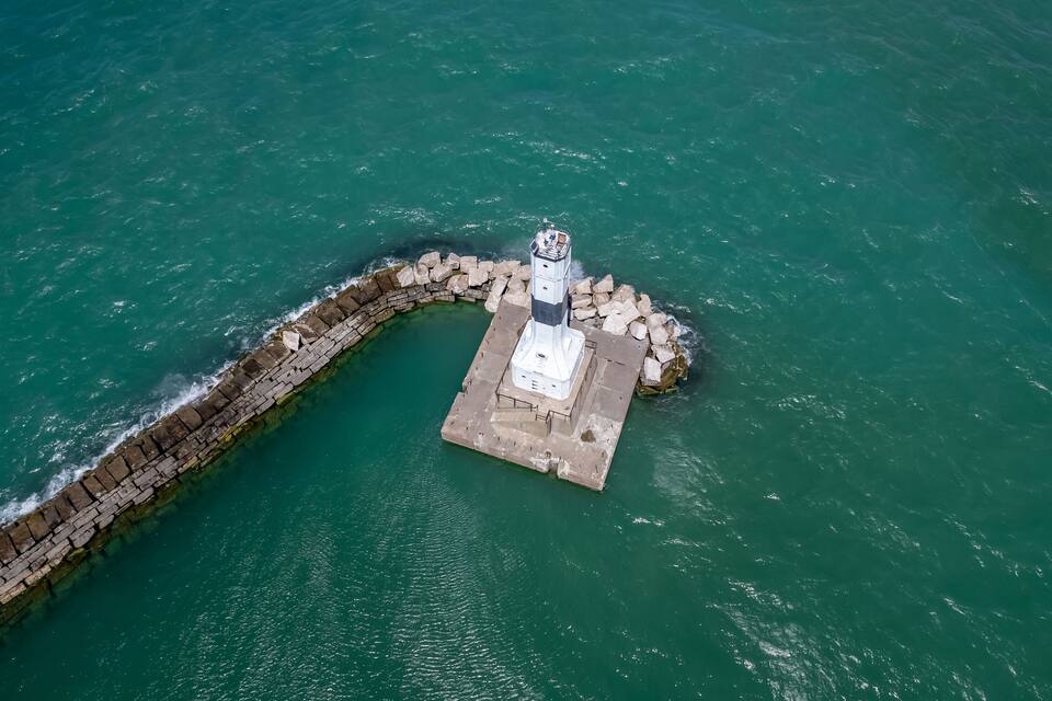 Luftaufnahme eines Leuchtturms auf einer kleinen Insel mit einem Steinmole.