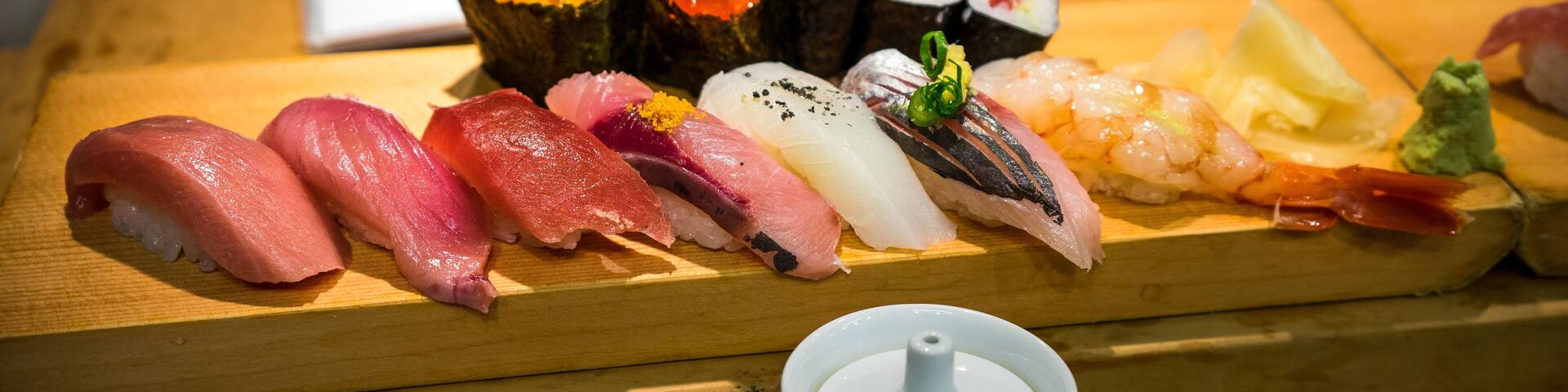 A wooden table with various types of sushi and sashimi, including salmon, tuna, and shrimp, along with a white teapot.
