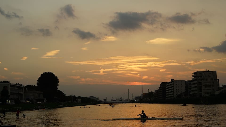 A sunset over a river with boats, buildings, and a bridge in the background.