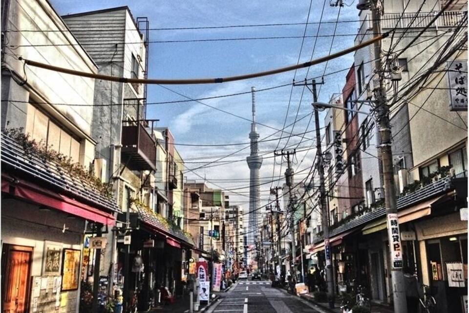 Rua com edifícios, uma torre ao longe e linhas de energia aéreas.