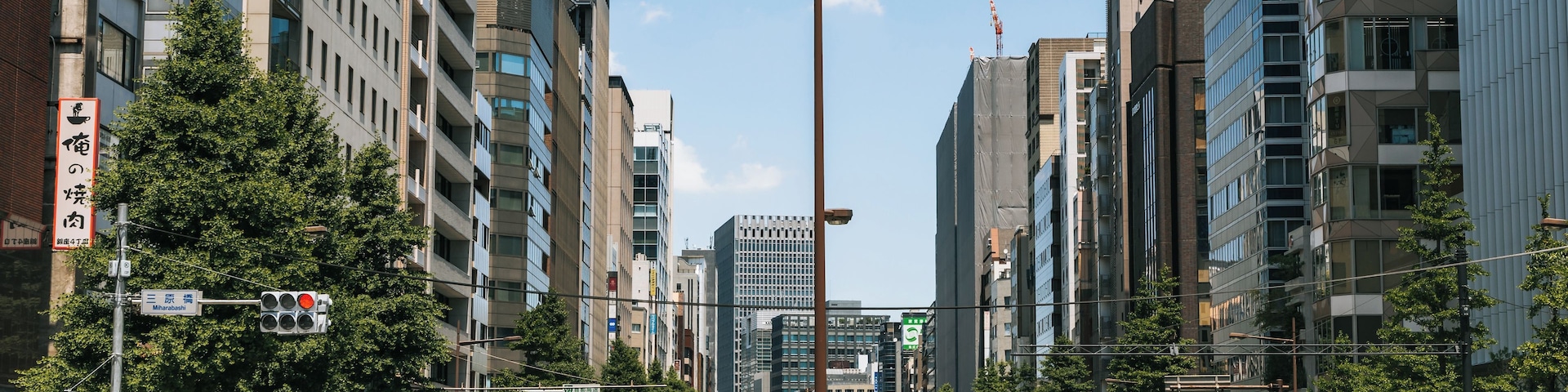 Uma rua urbana movimentada com edifícios modernos, semáforos e uma faixa de pedestres.