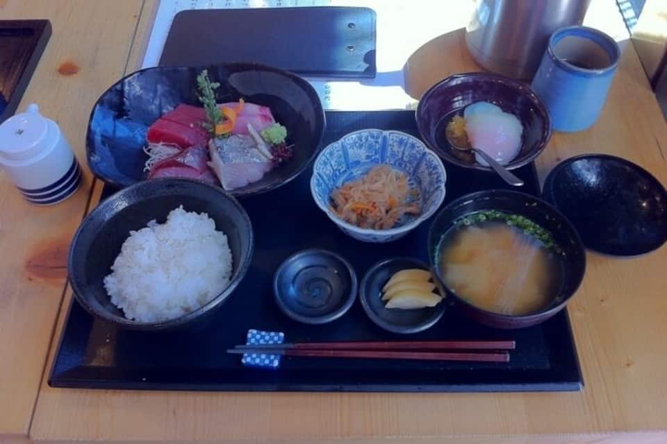 Una comida tradicional japonesa con arroz, sashimi, sopa de miso y verduras encurtidas sobre una bandeja.