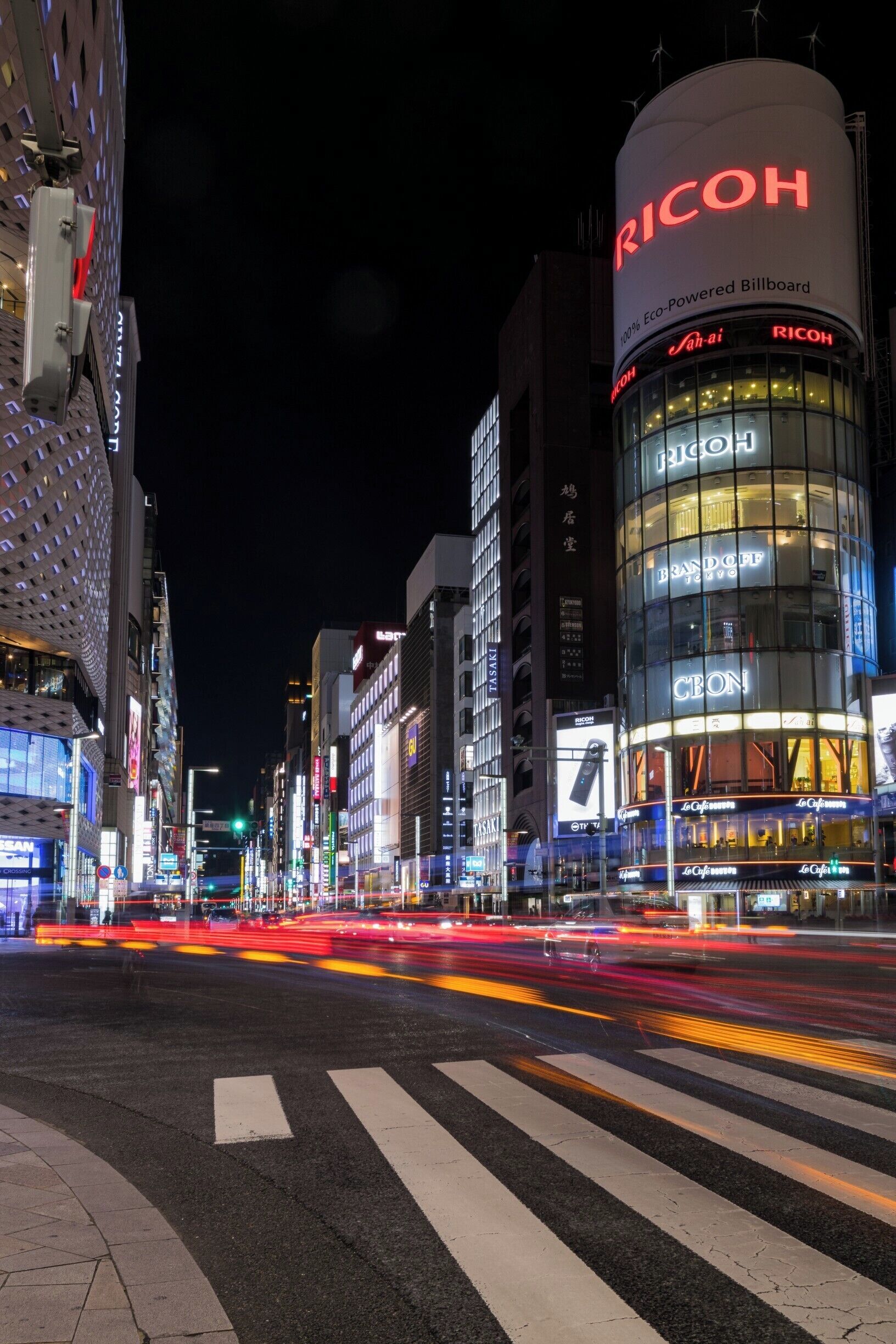 A brightly lit urban street at night with illuminated billboards and a prominent RICOH billboard.