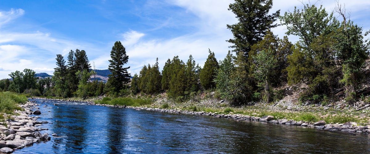 A river with clear blue water, surrounded by trees and rocks.