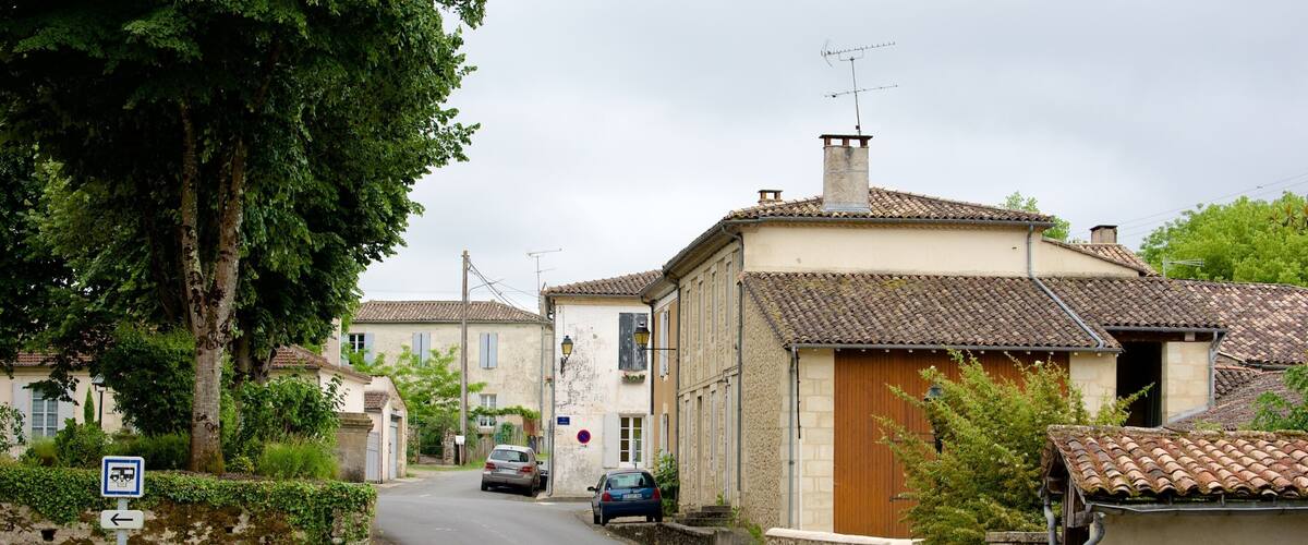 A narrow village street lined with traditional houses, a parked car, and a sign indicating a no parking zone.