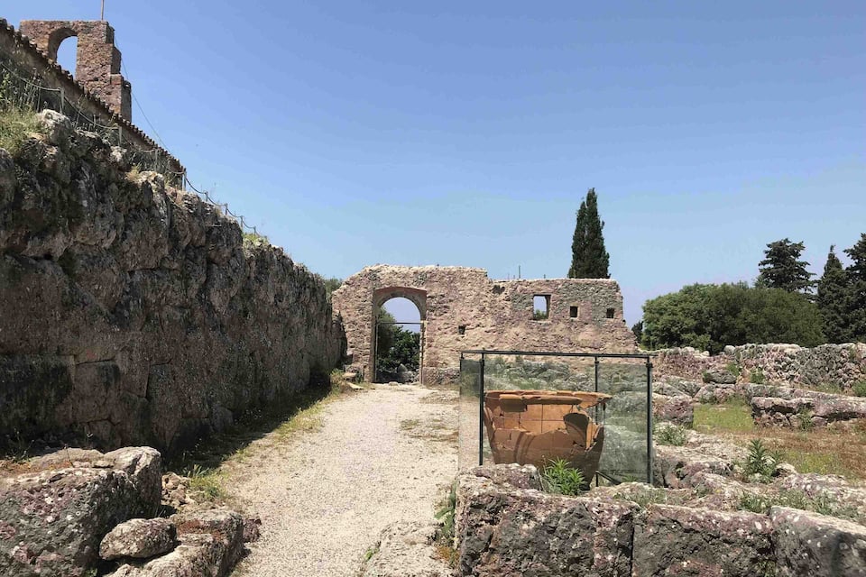 Ancient ruins with stone walls and archways, a clear sky, and a path leading through the site.