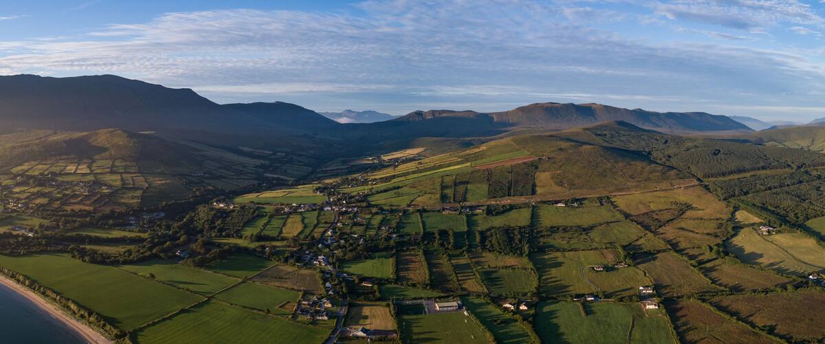 A coastal village with fields, a winding road, and mountains in the background.