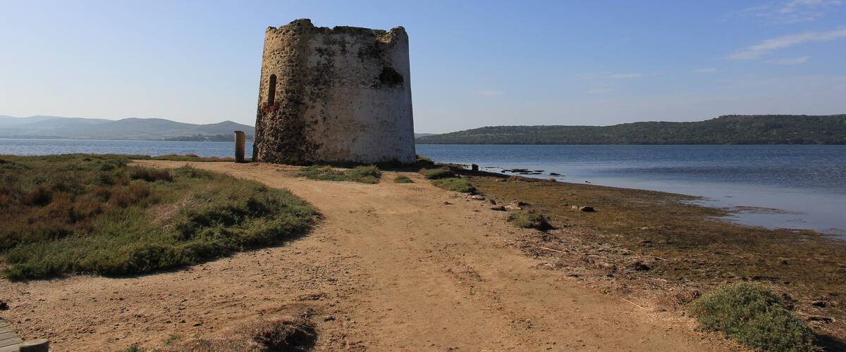A coastal tower by a lake with a dirt path leading to it.