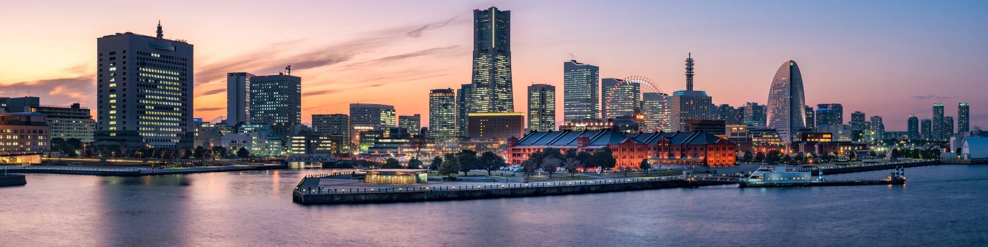 A city skyline at dusk with illuminated buildings and a waterfront.