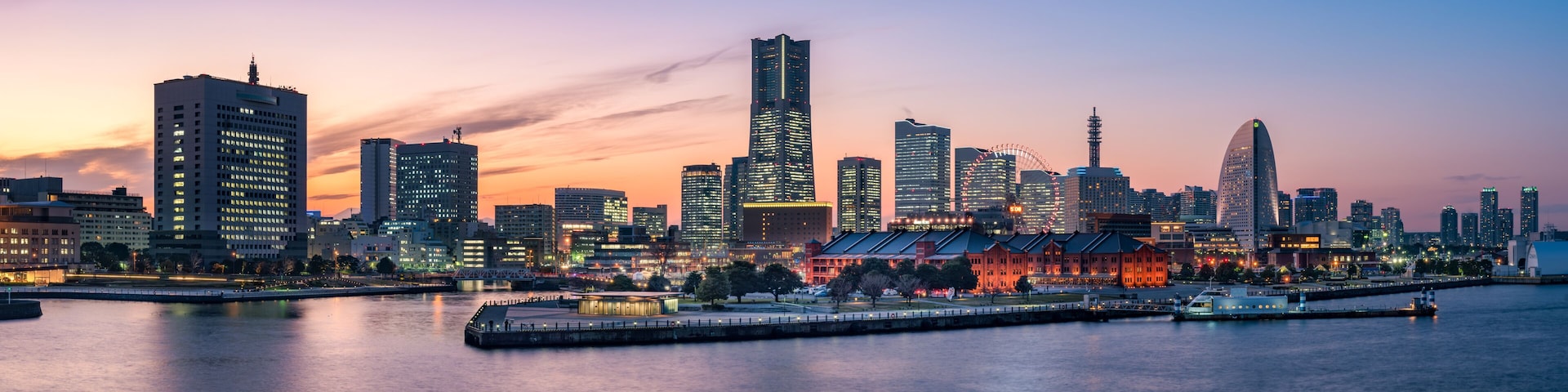 A city skyline at dusk with illuminated buildings and a waterfront.