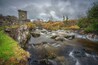 A stone bridge over a flowing river with a tower in the background.