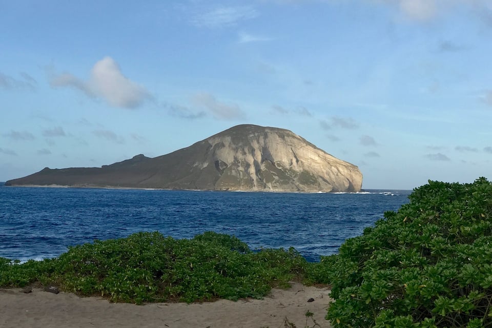 A large rock formation in the ocean with a sandy beach in the foreground.
