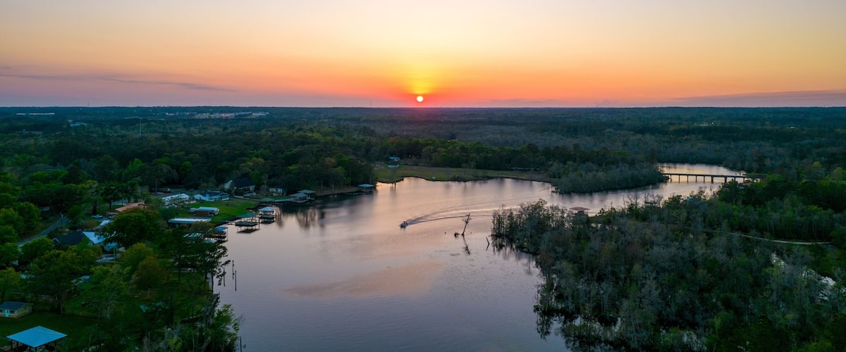 A sunset over a lake with a pier and surrounding greenery.