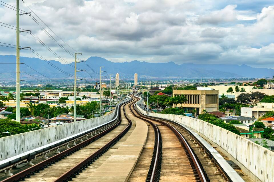A railway track with a bridge, urban buildings, and mountains in the background.