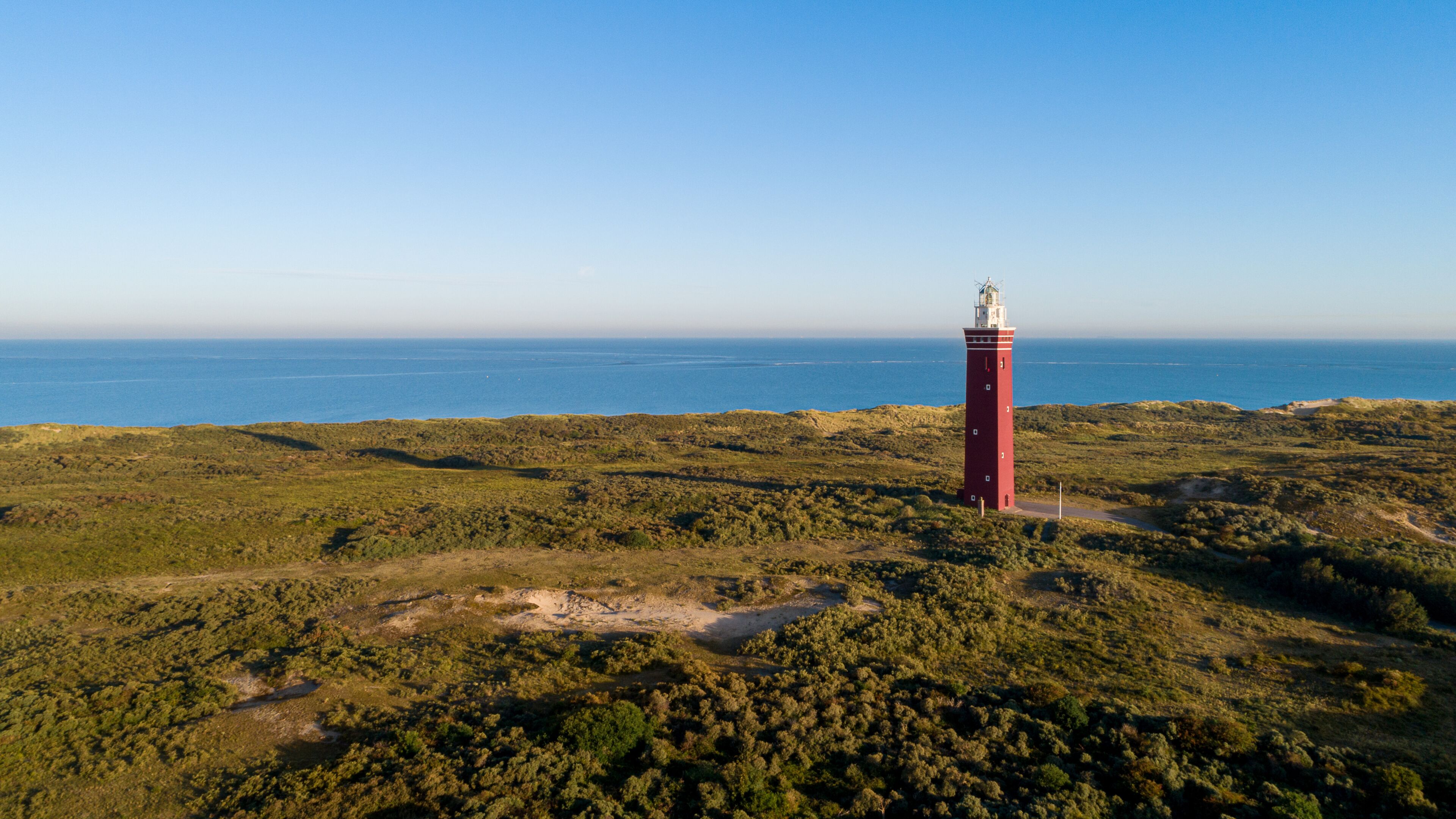 A red lighthouse on a grassy hill overlooking a coastal area.