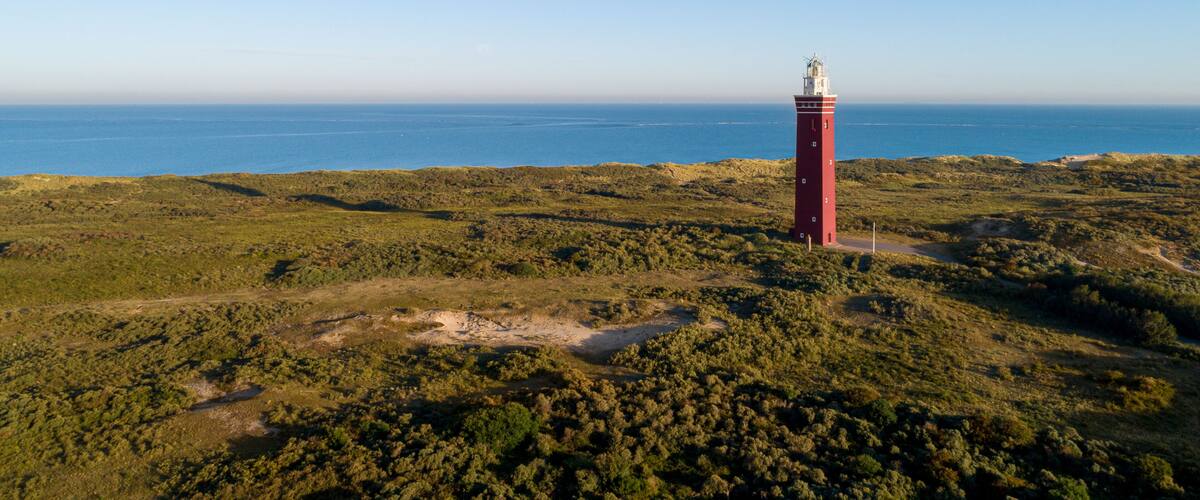 A red lighthouse on a grassy hill overlooking a coastal area.