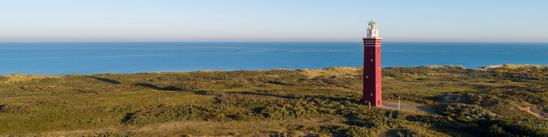 A red lighthouse on a grassy hill overlooking a coastal area.