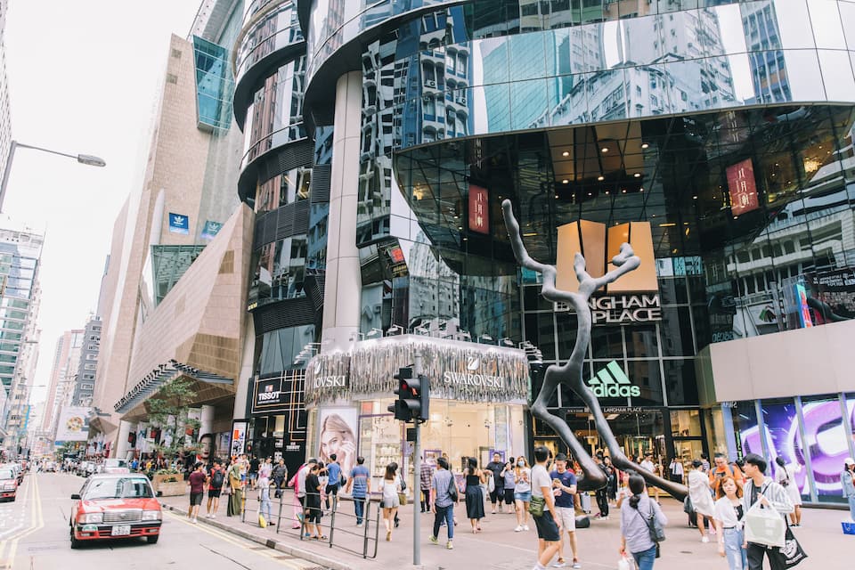 A busy urban street with modern buildings, including a Swarovski store and a Tissot store.