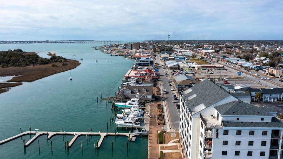 A coastal town with a marina, a bridge in the distance, and a mix of commercial and residential buildings.