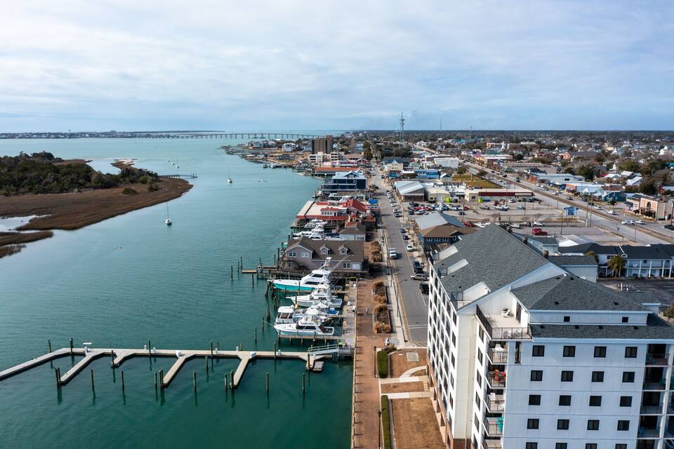 Uma vila costeira com um porto de recreio, uma ponte ao longe, e uma combinação de edifícios comerciais e residenciais.