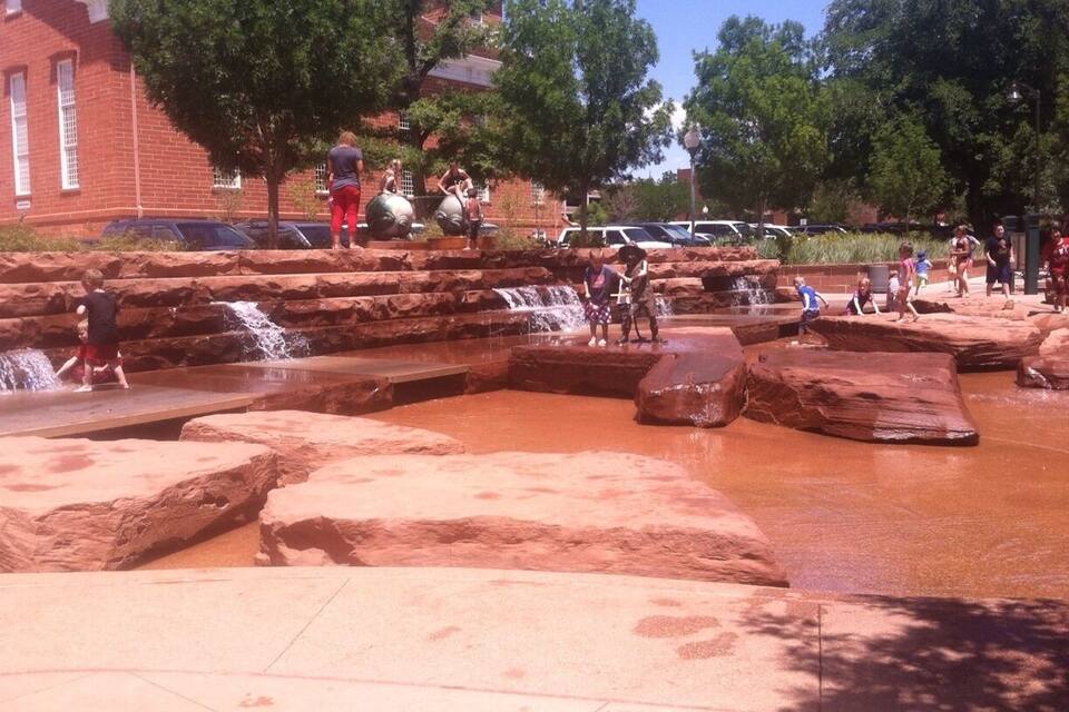 A water park with rock formations and a red brick building in the background.