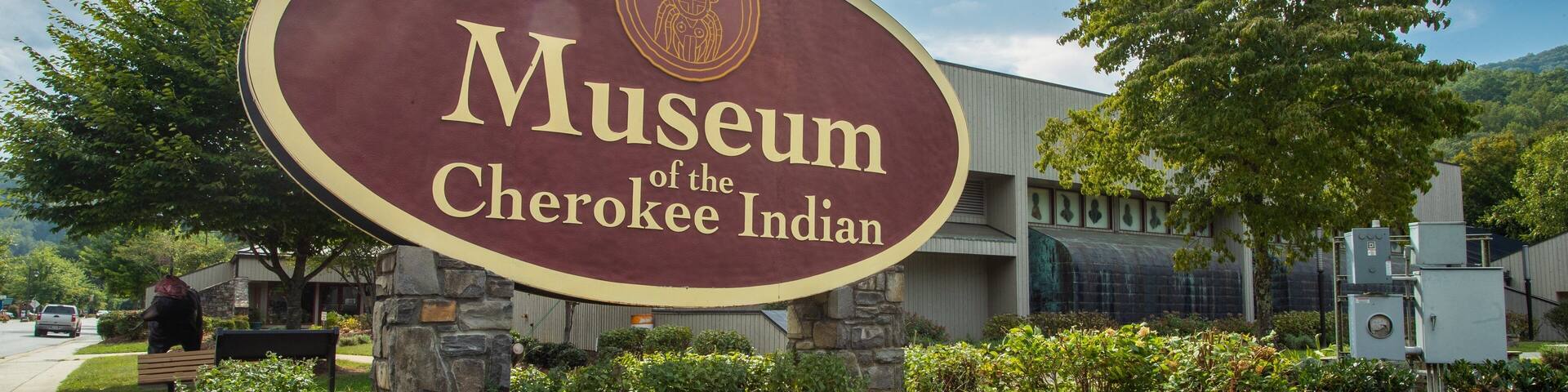 A sign for the Museum of the Cherokee Indian with a stone wall and greenery in the foreground.