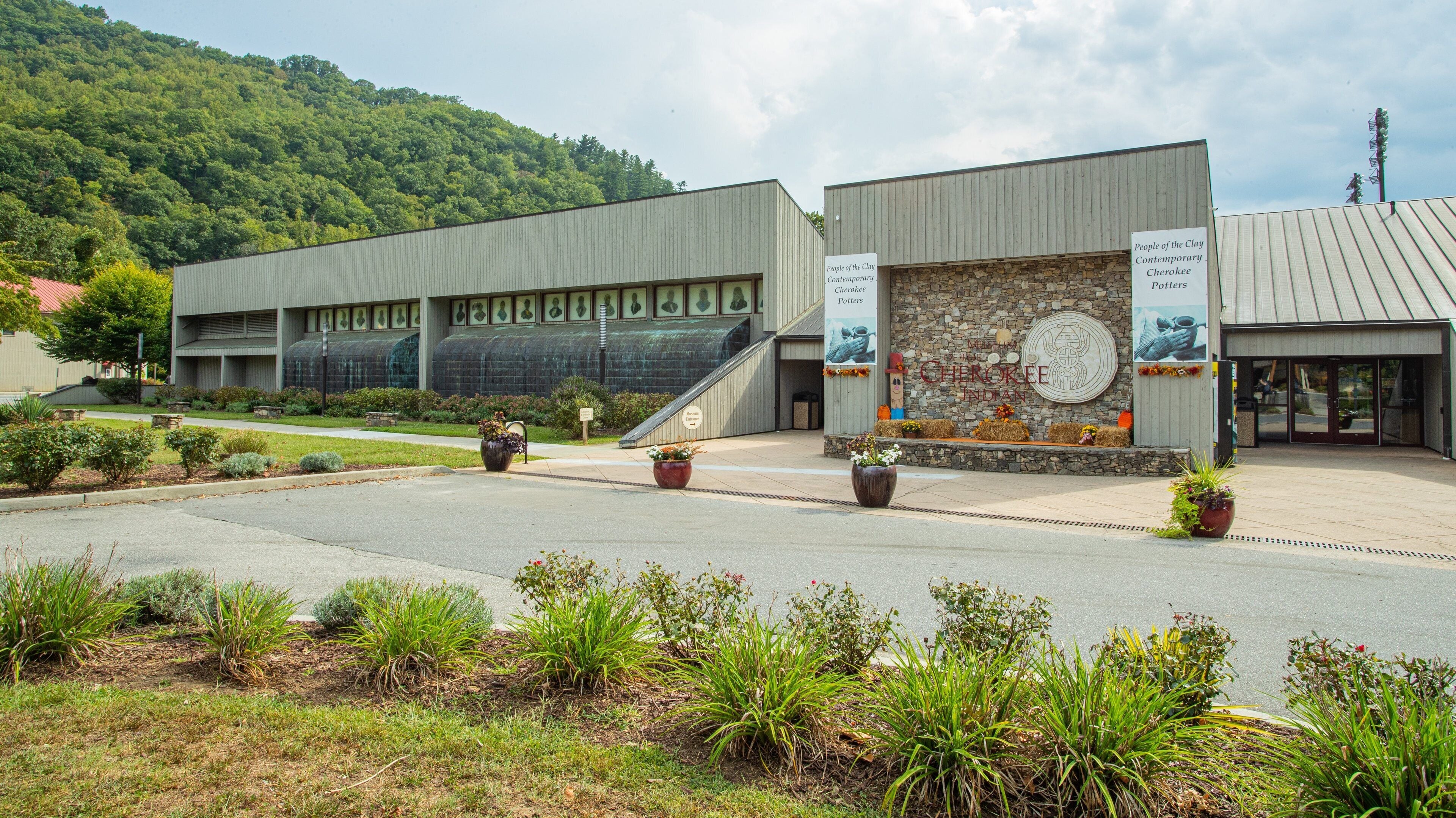 A museum with a large glass facade, a stone wall with a circular emblem, and a landscaped entrance area.