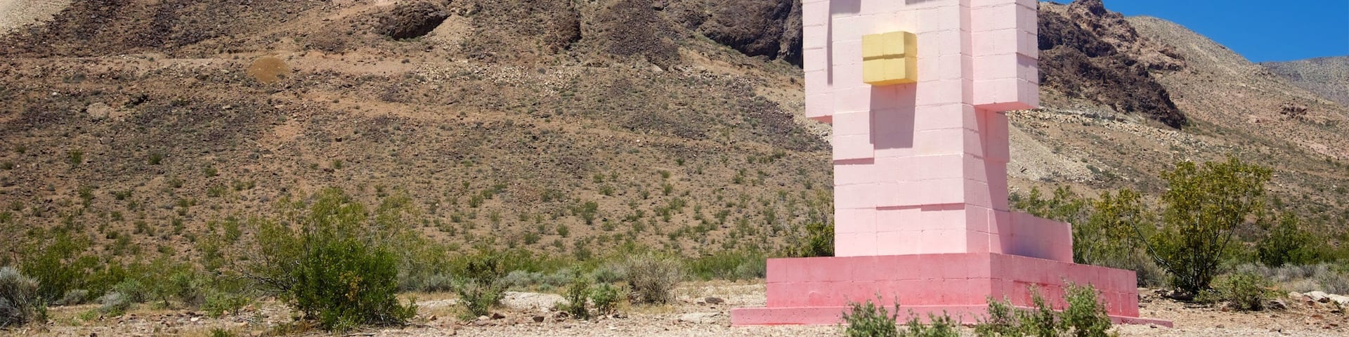 A pink and yellow monument in a desert landscape with a mountain in the background.
