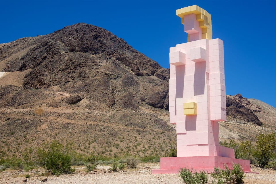 A pink and yellow monument in a desert landscape with a mountain in the background.