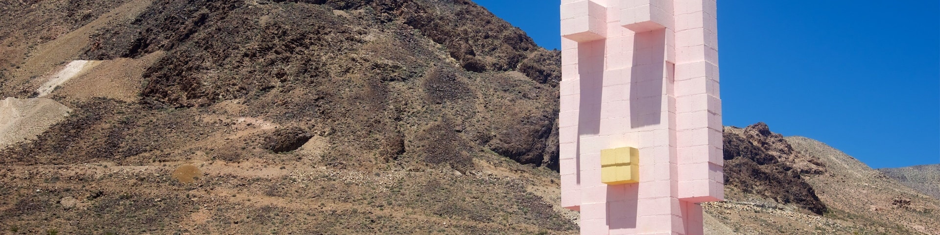 Un monumento rosa y amarillo en un paisaje desértico con una montaña al fondo.