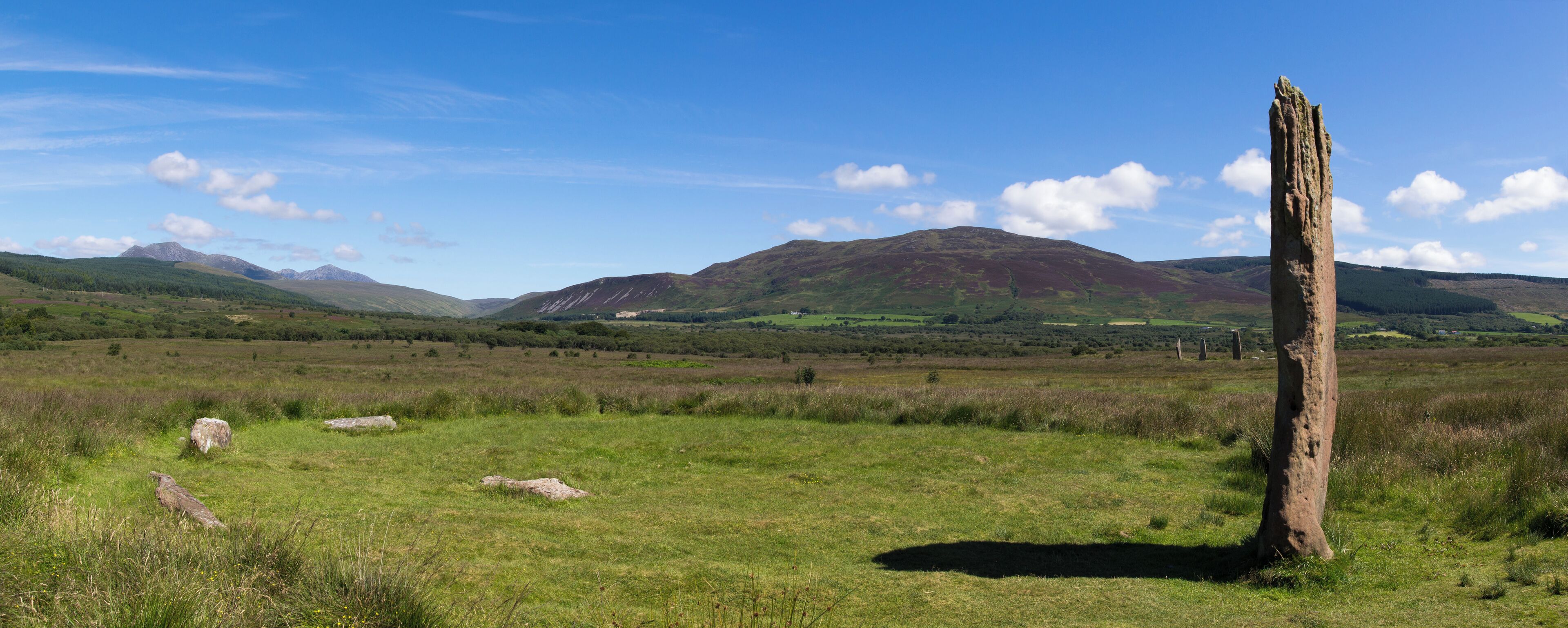 A grassy field with a standing stone and mountains in the background.