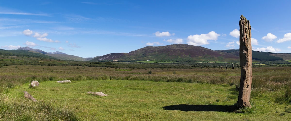 A grassy field with a standing stone and mountains in the background.