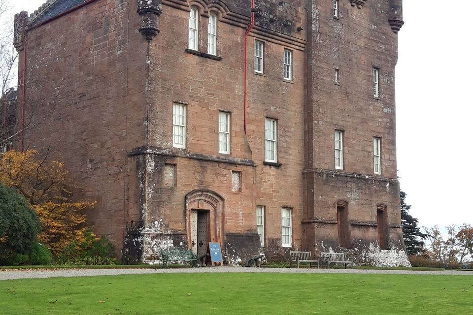 A large, historic brick castle with multiple towers and a well-maintained lawn in front.