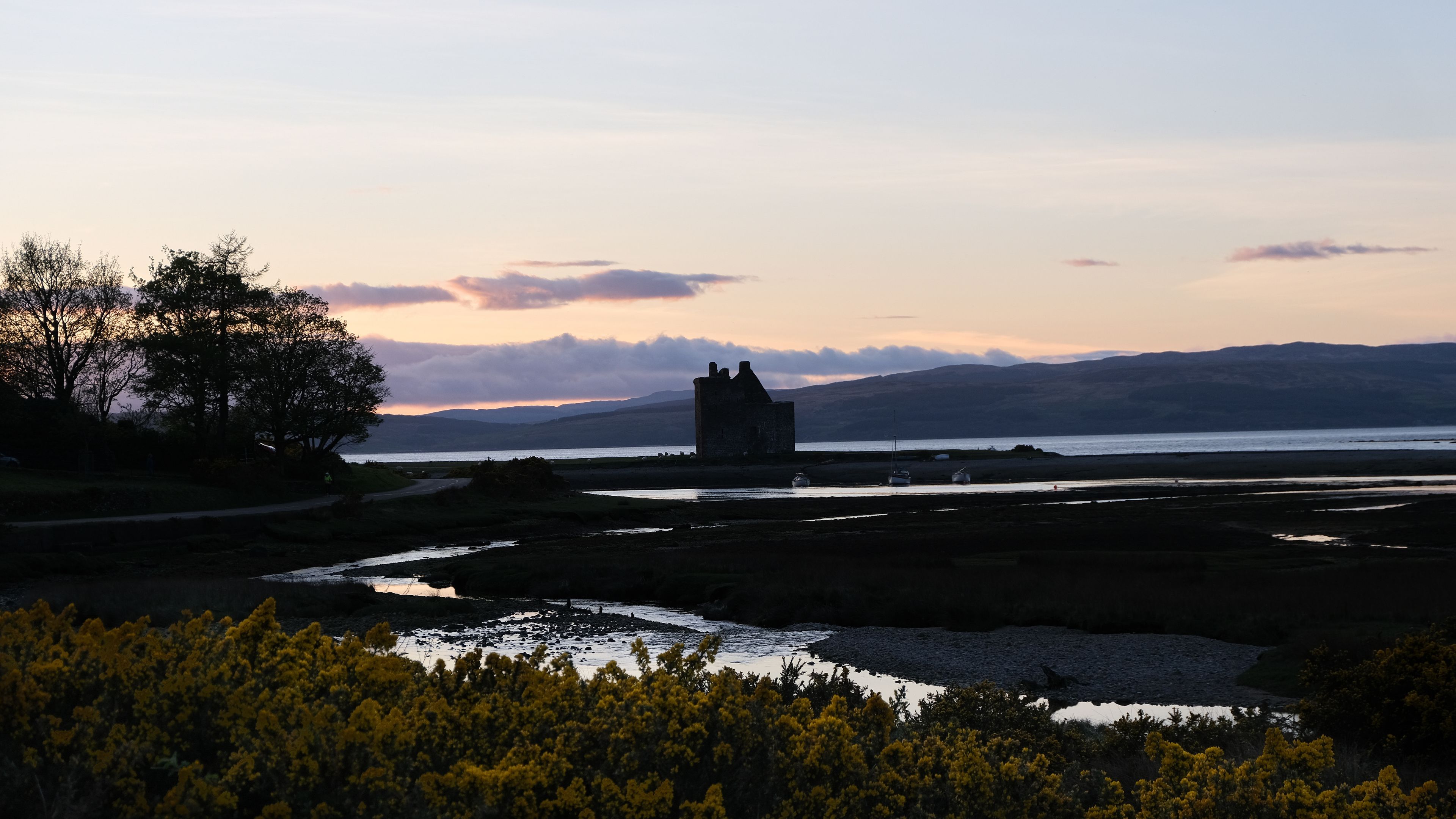 Silhouetted historical Scottish landmark of Lochranza Castle overlooking ocean and loch in rural countryside of Isle of Arran in Inner Hebrides, Scotland UK