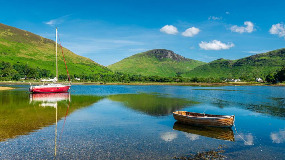 Un bateau et une barque attendant tranquillement dans le port de Lochranza en se reflétant sur l'eau, île d'Arran, Ecosse