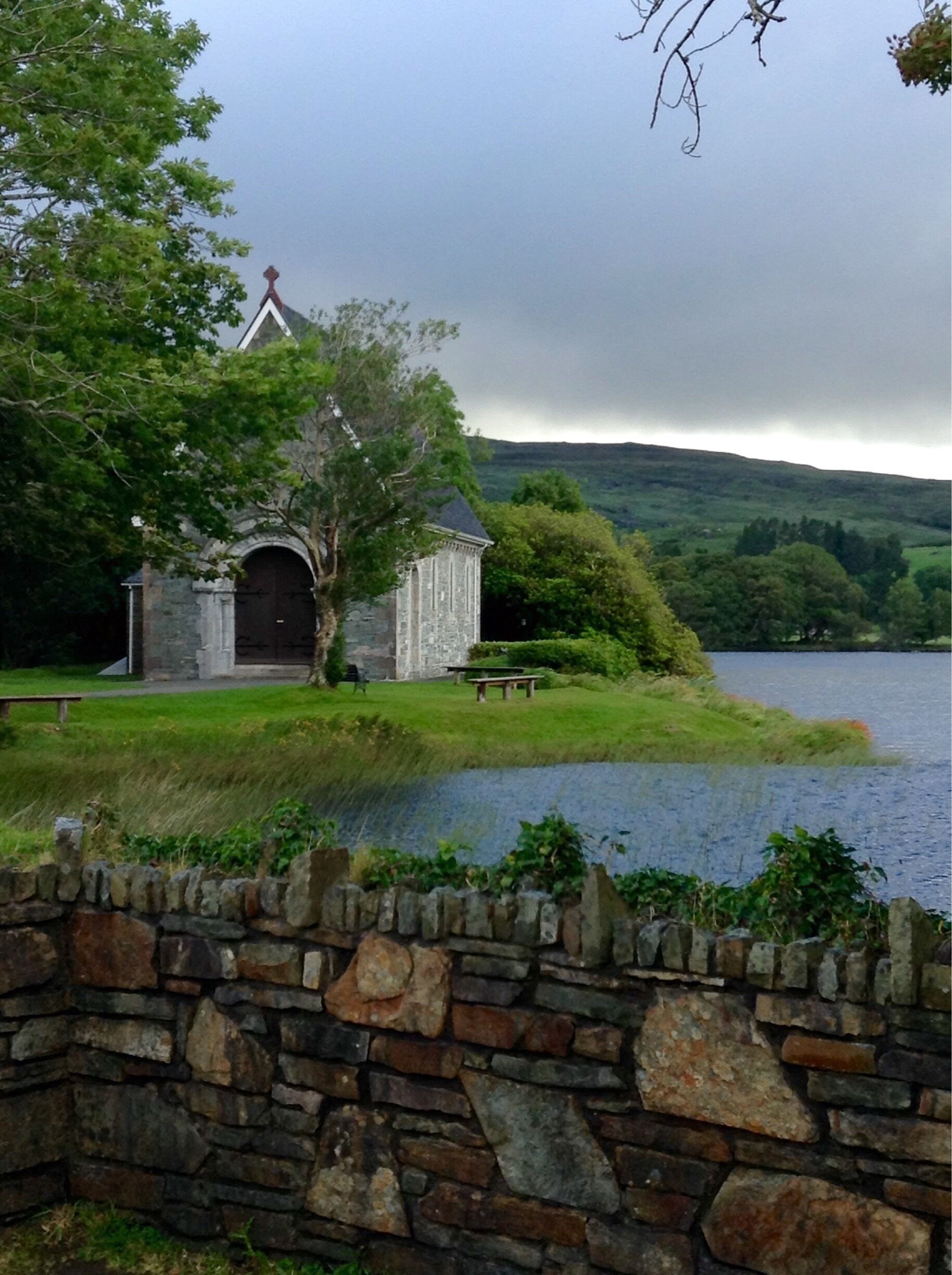A stone church with a bell tower by a lake.