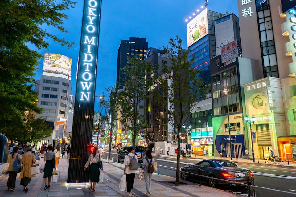 A busy urban street with people walking, cars, and illuminated buildings.