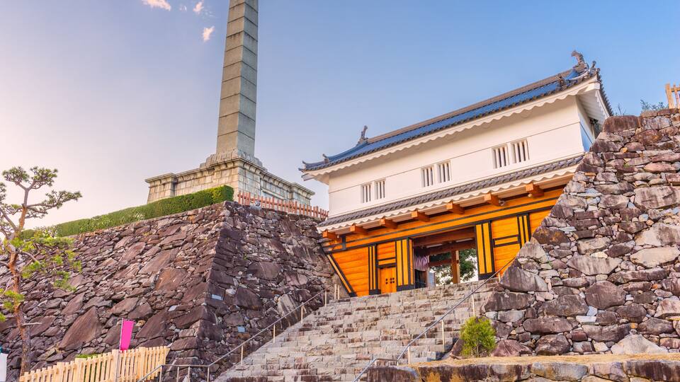 A traditional Japanese building with a stone staircase and a tall monument in the background.